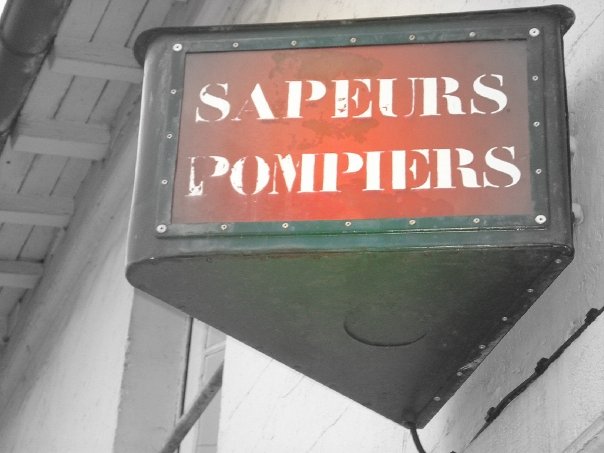 Enseigne historique verte avec lettres rouges « SAPEURS POMPIERS » sur façade de bâtiment.