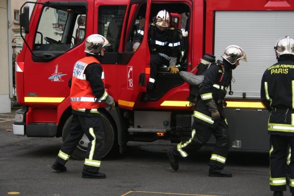 Pompiers en tenue et casques, partant en reconnaissance à partir d’un camion rouge de secours sur une intervention ou un attentat.